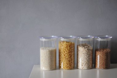  Gri arka planda cam kavanozlarda sağlıklı yemek pişirmek için çeşitli pişmemiş tahıllar.