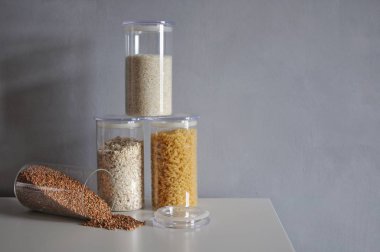  Gri arka planda cam kavanozlarda sağlıklı yemek pişirmek için çeşitli pişmemiş tahıllar.