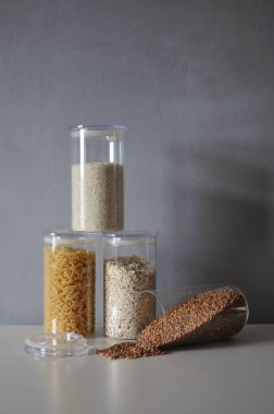  Gri arka planda cam kavanozlarda sağlıklı yemek pişirmek için çeşitli pişmemiş tahıllar.