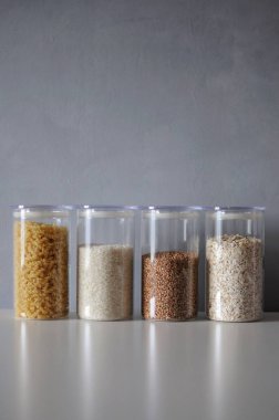  Gri arka planda cam kavanozlarda sağlıklı yemek pişirmek için çeşitli pişmemiş tahıllar.