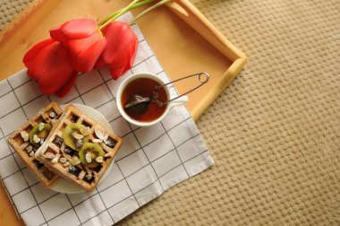 Belçika waffle 'ı, siyah çay ve kırmızı lalelerle yatakta kahvaltı 