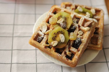 Beyaz havluda şekerle pudralanmış meyve ve granola ile ev yapımı Belçika waffleları