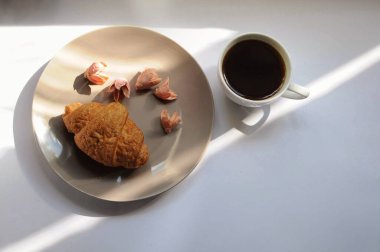 Kahveli ve çiçekli kruvasan tabakta. Gölgeli üst manzara kahvaltısı.