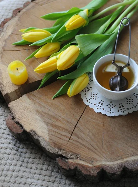 Enjoying breakfast in bed with cup of tea and yellow tulips on wooden table — Stock Photo, Image