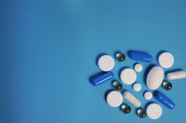 Mavi arka plan ve renkli haplar. Bir sürü renkli hap, antiviral ilaçlar da dahil. COVID-19 ve diğer hastalıklara karşı ilaçlar