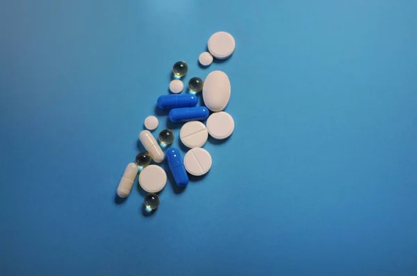 Много разных таблеток на голубом столе. Лекарство от COVID-19 и болезней — стоковое фото