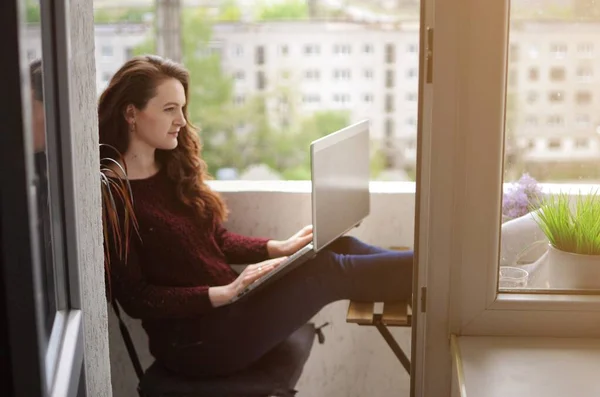 Girl freelancer working on a laptop on balcony during corona virus quarantine. Work from home. Remote education.