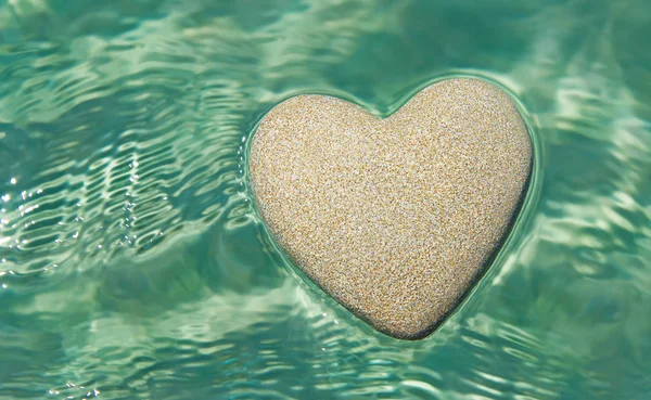 Herz aus Sand schwimmt in transparentem Ozean Wellen Wasser b — Stockfoto