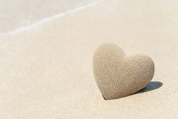 Cuore di sabbia con ombra su sfondo spiaggia sabbiosa contro — Foto Stock