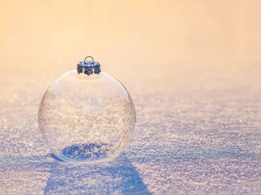 Günbatımında kar taneleri parlayan camdan bir Noel topu.