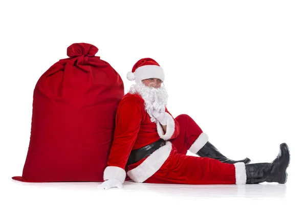 Santa Claus sentado cerca de un enorme saco rojo de Navidad lleno de regalos a — Foto de Stock