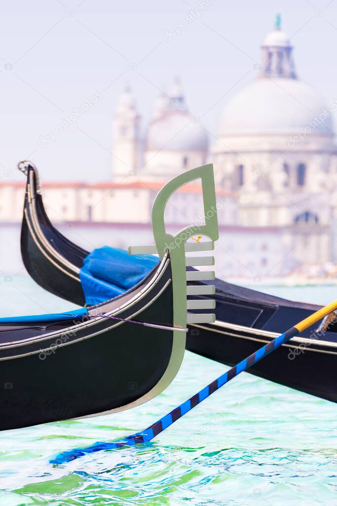 A gondolas tour on Grand Canal against Basilica di Santa Maria della Salute background, Venice, Italy,vertical cityscape. Iron prow-head with dinosaur and striped oar close-up as iconic symbol of city