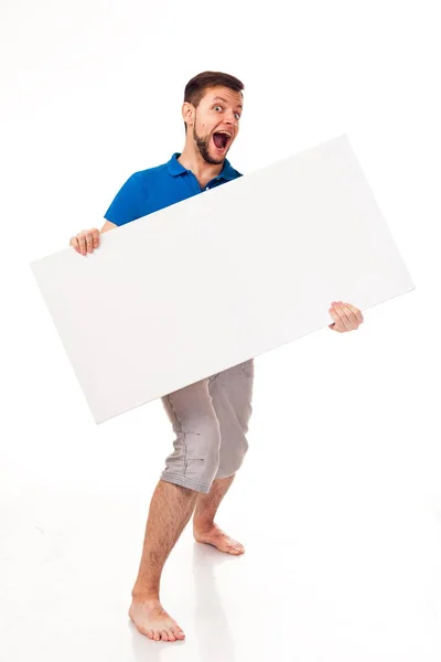 一个留着胡子的男人和一个白色的牌子可用于放置广告 徽标等 穿着蓝色的 T恤和灰色的裤子 — 图库照片