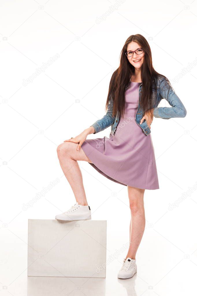 Young beautiful girl posing with white background for posting advertising, logo. Dressed in a pink dress and denim jacket, sneakers and glasses. Long hair. Isolated photo on the white background.