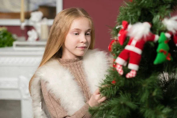 暖炉とクリスマス ツリーの近くの白い椅子に座っておもちゃを抱いて美しいクリスマスの女の子 — ストック写真
