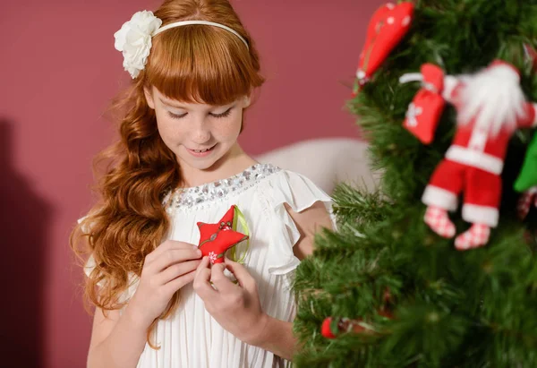 La chica en el lado de la chimenea blanca, decorar un árbol de Navidad con juguetes —  Fotos de Stock