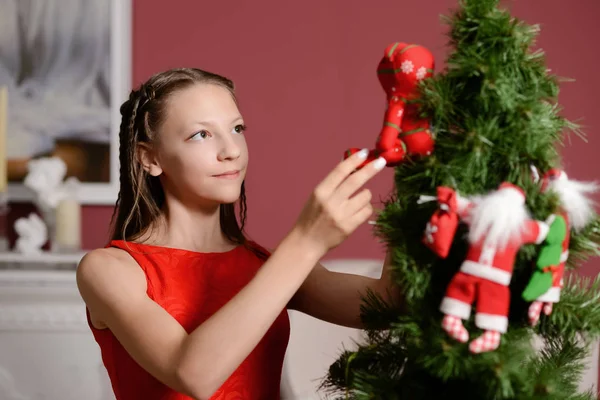 La chica en el vestido rojo al lado de la chimenea blanca, decorar un árbol de Navidad con juguetes —  Fotos de Stock