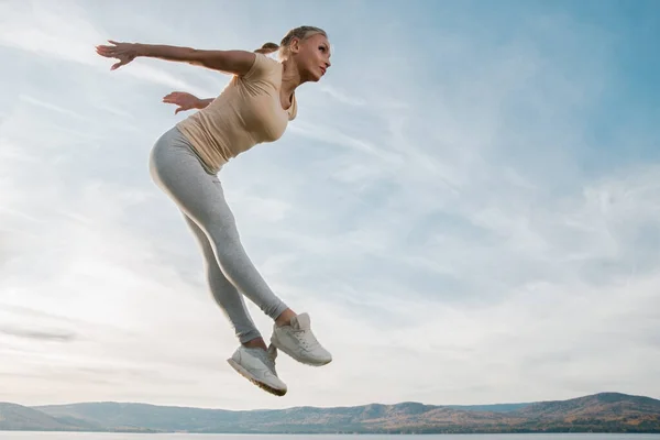 beautiful woman fitness instructor jumps on the sky background