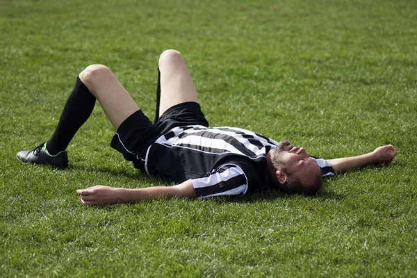 Футболіст лежить на траві Стокове Зображення