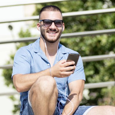 Kulaklık takan gülümseyen adam telefonu kullanıyor.