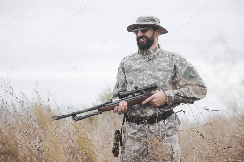 The smiling hunter or rifleman with shotgun or air gun is standing in nature.