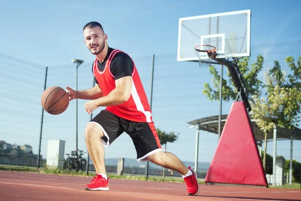 The young basketball player is playing basketball or streetbasket outdoors on playing field.