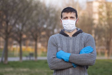 Parkta koruyucu maskeli ve koruyucu eldivenli bir adamın portresi..