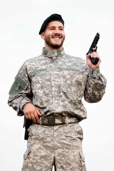 身穿军装 面带微笑的士兵手里拿着一支白色背景的手枪 — 图库照片