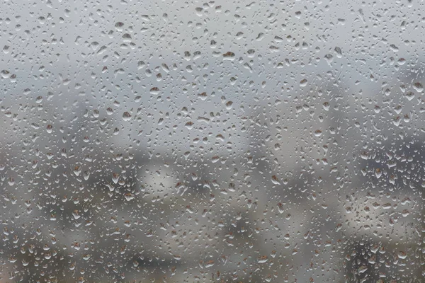 Lluvia cae en la ventana, sobre el fondo borroso de una ciudad —  Fotos de Stock