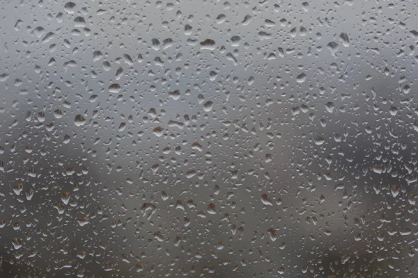 Chuva cai na janela, contra o fundo embaçado de uma cidade — Fotografia de Stock