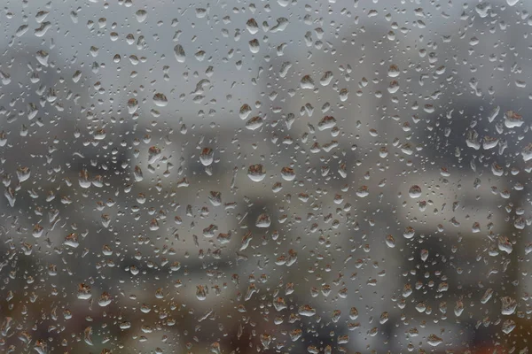 Chuva cai na janela, contra o fundo embaçado de uma cidade — Fotografia de Stock
