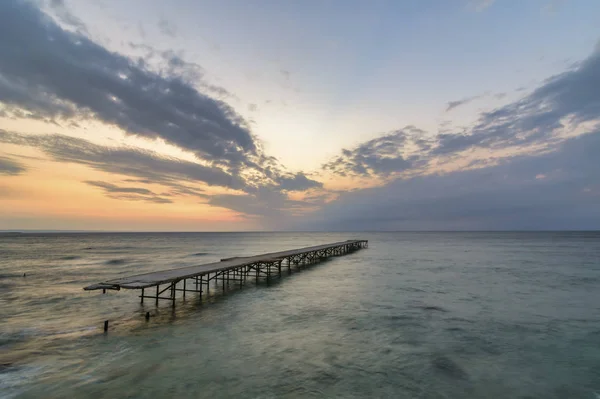 Ponte quebrada de concreto no mar contra um nascer do sol vibrante em V — Fotografia de Stock