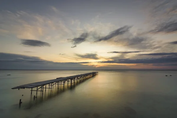 Ponte quebrada de concreto no mar contra um nascer do sol vibrante em V — Fotografia de Stock