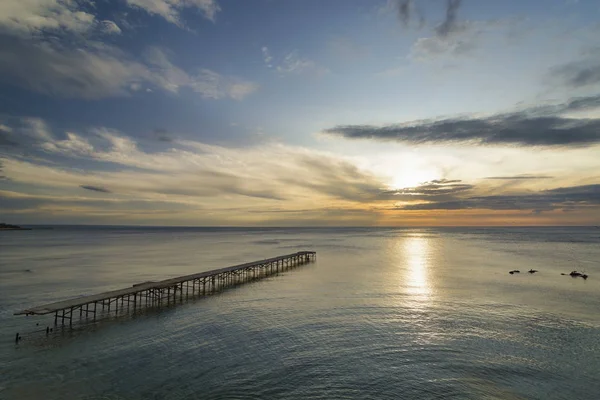 Ponte quebrada de concreto no mar contra um nascer do sol vibrante em V — Fotografia de Stock