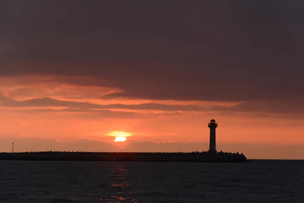 Bir deniz feneri gündoğumu canlı turuncu gökyüzü karşı deniz manzarası — Stok fotoğraf