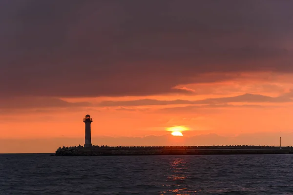 Paisagem marinha de um farol ao nascer do sol contra um céu laranja vibrante — Fotografia de Stock