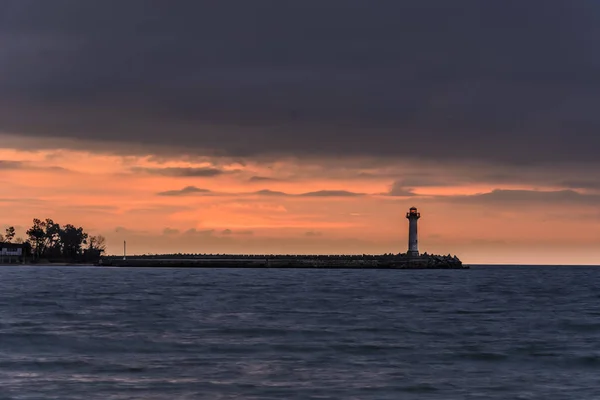 Paisagem marinha de um farol ao nascer do sol contra um céu laranja vibrante — Fotografia de Stock
