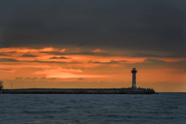 Paisagem marinha de um farol ao nascer do sol contra um céu laranja vibrante — Fotografia de Stock