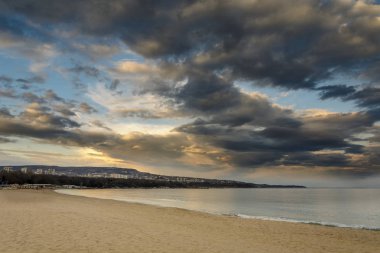 Gün batımı, dramatik bulutlar denize kumsalda.