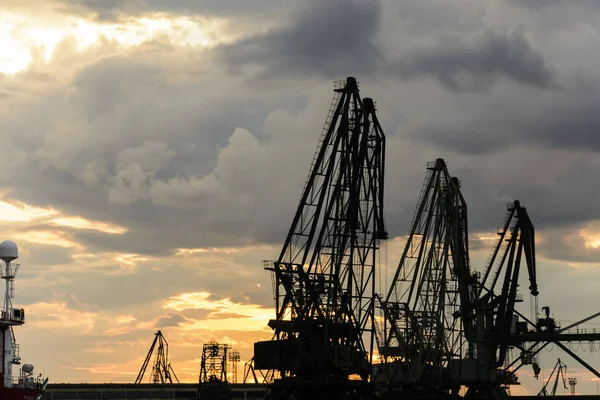 Silhouette of port cranes against a dramatic sky at sunset.