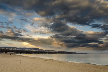Gün batımı, dramatik bulutlar denize kumsalda.