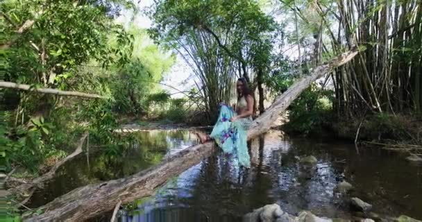 Chica balanceando su pierna en un tronco de árbol en la parte superior de un río — Vídeo de stock