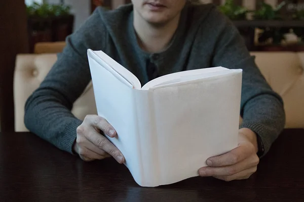 Un hombre en una mesa en un café leyendo un libro en cubierta blanca — Foto de Stock