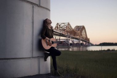 girl with a guitar standing at the foot of the bridge over the r clipart
