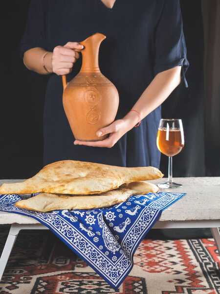 delicious georgian lavash with glass of beverage and person holding clay jug behind