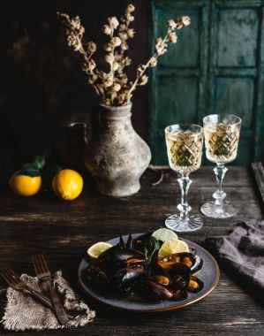 Cooked mussels with shells served on plate with two glasses of white wine on wooden table clipart
