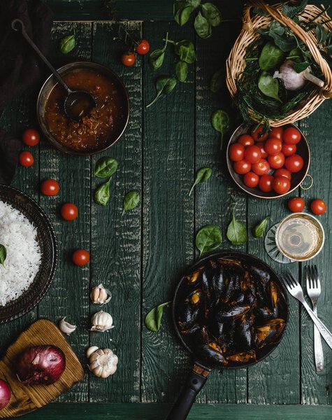 Top view of cooked mussels with shells served in pan with tomatoes, herbs and wine on rustic table