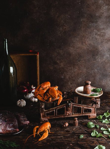 close-up view of delicious lobsters on vintage scales, raw fish and basil leaves on rustic table top  