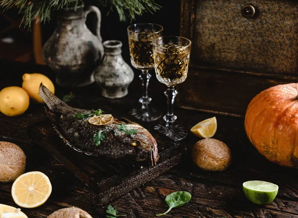 Baked fish with lemon and herbs on wooden board with white wine glasses on dark wooden table — Stock Image Baked Fish Lemon Herbs Wooden Board White Wine Glasses Dark Royalty Free Stock Images