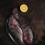 Top view of raw fresh fish on vintage plate with half of lemon and fennel on dark table top